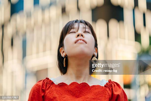 portrait of young woman closing her eyes and looking up in city - japanese bussiness woman looking up imagens e fotografias de stock
