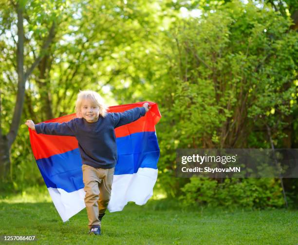 Portrait of cute little boy in public summer park with russian flag on background. Fans child supporting and cheering theirnational team. Day of independence.