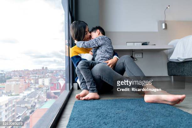 latino mother and son sitting on the floor looking out the window - battered child syndrome stock pictures, royalty-free photos & images