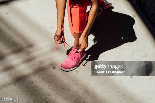 fit afrikaanse sportvrouw in rode sportkleding koppelverkoop schoenveters tijdens een city run - necktie run stockfoto's en -beelden
