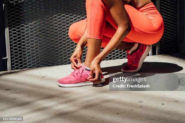 mujer deportiva africana de ajuste irreconocible en red sportswear tying shoelaces en zapatillas durante una carrera de la ciudad - pink sneakers fotografías e imágenes de stock