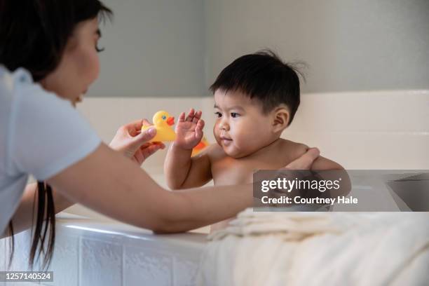 adorable baby boy plays with rubber duck while his mother gives him a bubble bath - baby bath toys stock pictures, royalty-free photos & images