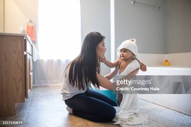 baby berührt mütter gesicht, während sie ihn in ein handtuch nach einer blase bad im badezimmer wickelt - kid bath mother stock-fotos und bilder