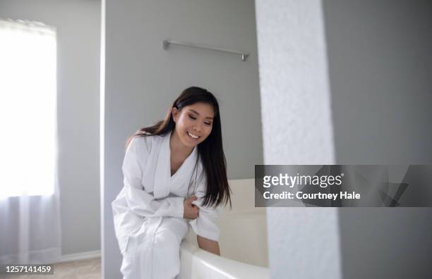 beautiful young asian woman smiles while running bath water in her bathroom and wearing a robe - beautiful filipino women stock pictures, royalty-free photos & images