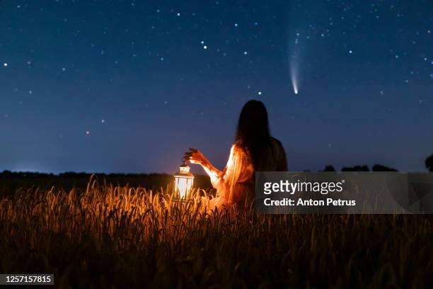 woman in field with lantern on background of comet neowise c/2020 f3 - vinden stockfoto's en -beelden