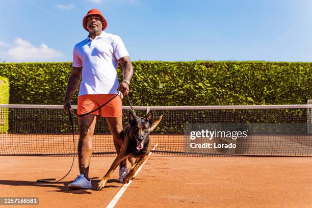 a handsome black middle aged male tennis player and his dog on the court - amateur tennis man stock pictures, royalty-free photos & images