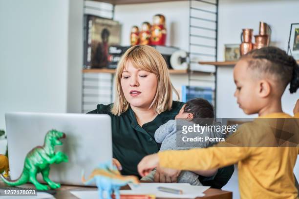 madre trabajadora con recién nacido mientras el hijo juega en casa - leanincollection working mom fotografías e imágenes de stock