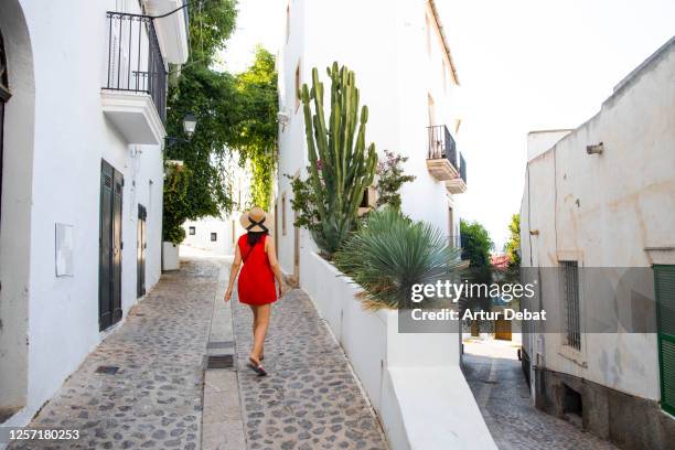woman in red dress walking in the old city of the ibiza town with summer style and white houses. mujer con vestido rojo en la parte antigua del pueblo de ibiza con casas blancas. - mujer fashion bildbanksfoton och bilder
