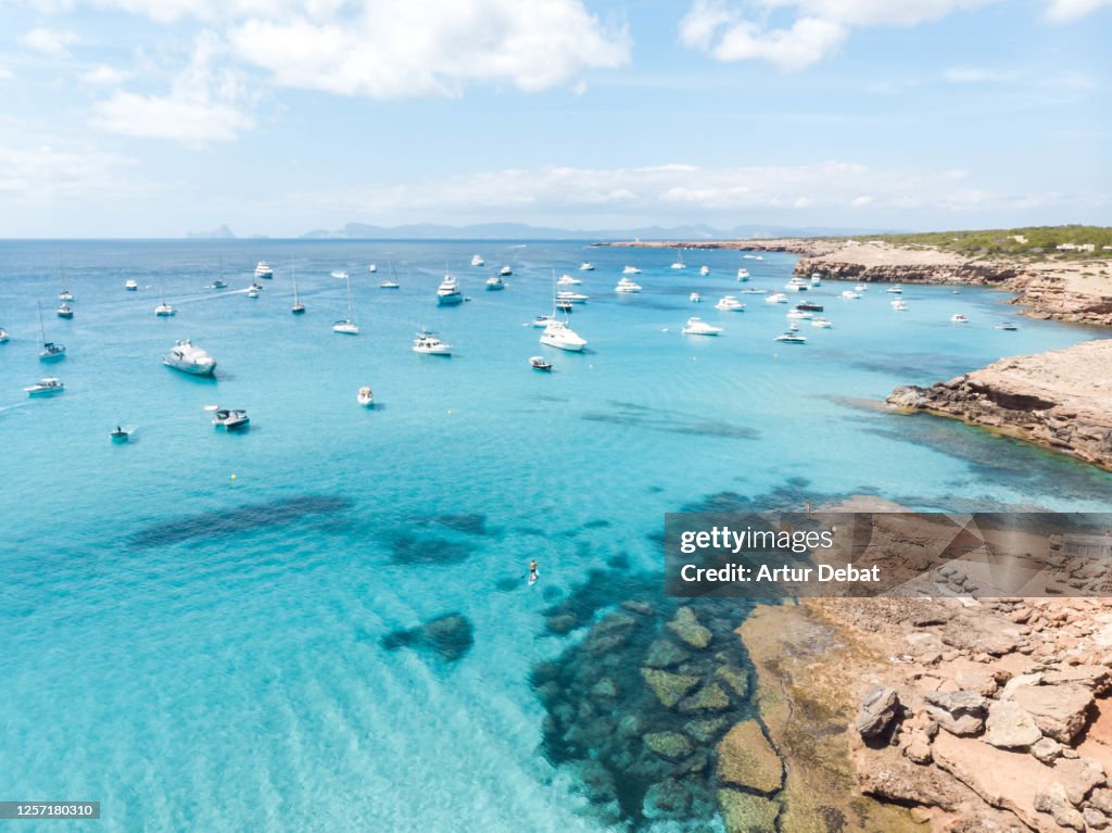 Aerial view of the Formentera island with paradise beach and yachts in the Mediterranean Sea with the Ibiza island silhouette. Toma aérea de la isla de Formentera con playas paradisiacas y yates.