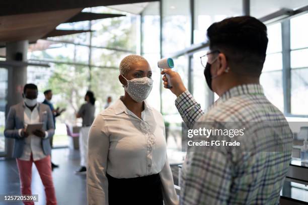 receptioniste die temperatuur van vrouwelijke werknemer bij de ingang van het bureau meet - met gezichtsmasker - screening of 20th century foxs ferdinand arrivals stockfoto's en -beelden