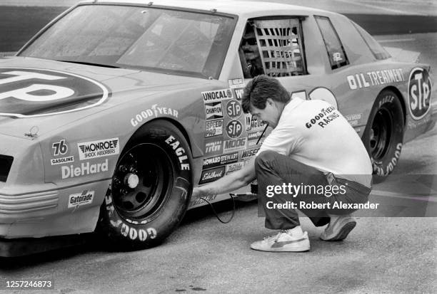 Goodyear Racing worker checks the tire pressure on NASCAR driver Richard Petty's racecar during a practice session prior to the start of 1982...