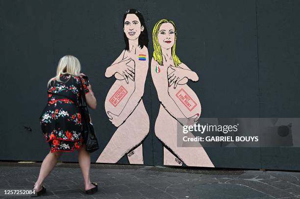 Pedestrian takes a picture of a mural painting made by Italian artist and activist aleXsandro Palombo, depicting Prime Minister Giorgia Meloni and...