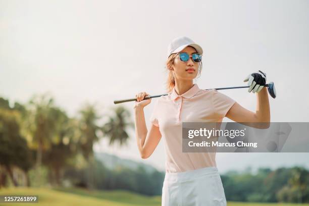 porträt einer asiatischen chinesischen golferin, die den golfclub auf dem platz hält - polohemd stock-fotos und bilder