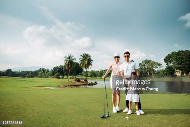 wide shot of asian chinese young smiling parent teaching daughter to playing golf at the golf course - family golf stock pictures, royalty-free photos & images