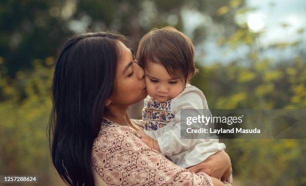 mom kissing baby's cheek outside - filipino mother baby stock pictures, royalty-free photos & images