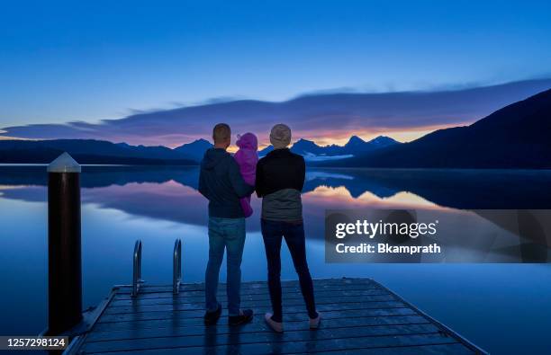 family take in a vibrant sunrise in the beautiful natural scenery of glacier national park's lake mcdonald area during the summer in montana, usa. - montana moody sky stock pictures, royalty-free photos & images