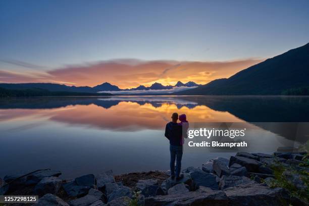 father and daughter looking at a vibrant sunrise in the beautiful natural scenery of glacier national park's lake mcdonald area during the summer in montana, usa. - montana mountains imagens e fotografias de stock