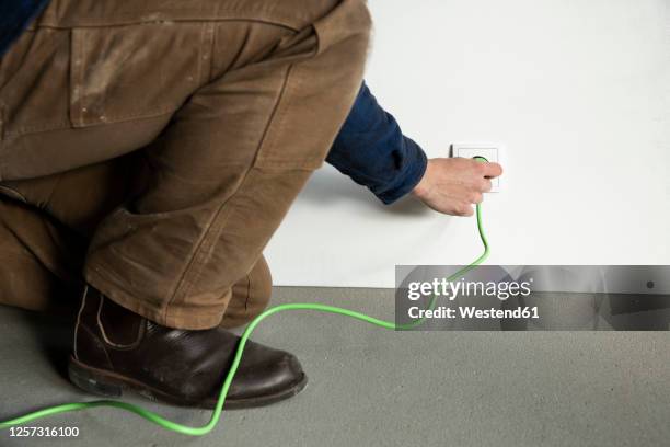close-up of male engineer inserting plug in outlet at constructing house - male feet imagens e fotografias de stock