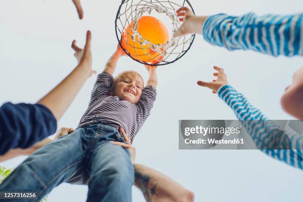 happy boy putting basketball in hoop while playing with family against clear sky - child and unusual angle stock pictures, royalty-free photos & images