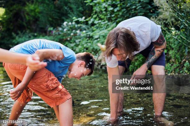 man exploring with boy in stream water at forest - com os pés na água imagens e fotografias de stock