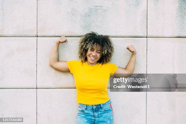 portrait of smiling strong woman on wall - yellow shirt stock pictures, royalty-free photos & images