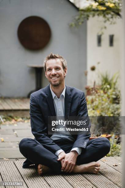laughing businessman sitting cross-legged in backyard - schneidersitz stock-fotos und bilder