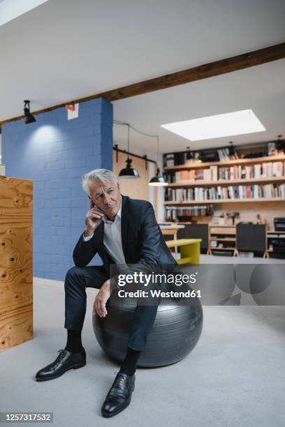 senior businessman sitting on fitness ball, thinking - gymnastikball stock-fotos und bilder