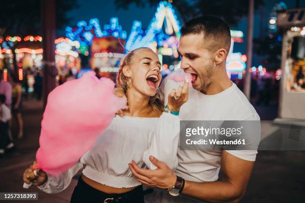 cheerful young woman feeding cotton candy to boyfriend at amusement park - eating candy stock-fotos und bilder