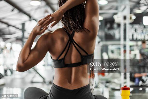 female athlete stretching hands while sitting in gym - dorsale foto e immagini stock
