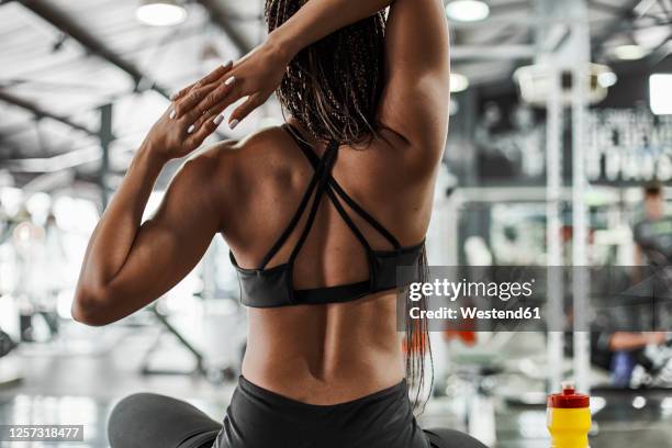 female athlete stretching hands while sitting in gym - back stretch stockfoto's en -beelden