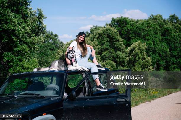 smiling woman sitting with dog on roof during sunny day - car roof stock pictures, royalty-free photos & images