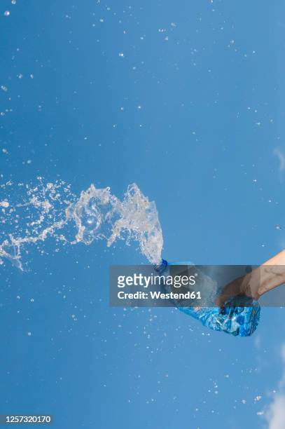 hand of woman splashing water from bottle against blue sky - water bottle splash stock pictures, royalty-free photos & images