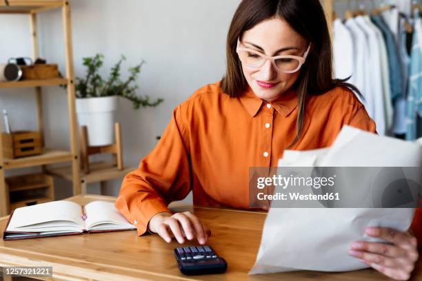 female freelancer working at home sitting at desk using calculator - accounting calculator stock pictures, royalty-free photos & images