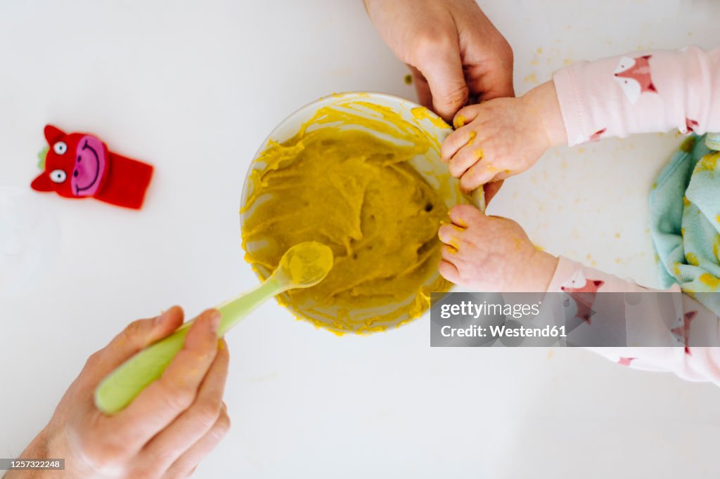 Father with spoon and baby girl touching bowl with baby food