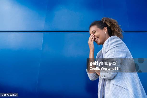 laughing businesswoman in front of blue wall - ironia imagens e fotografias de stock