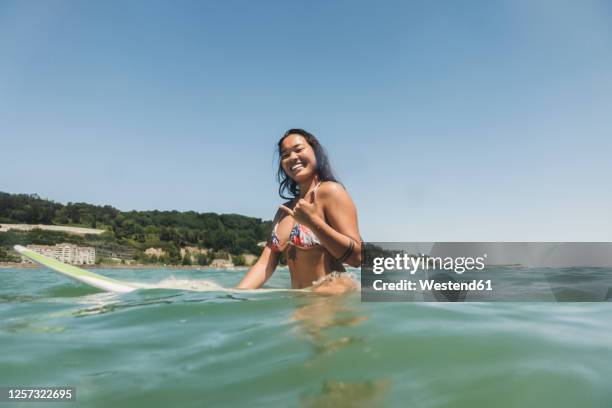 female surfer sitting on surfboard - shaka sign stock-fotos und bilder