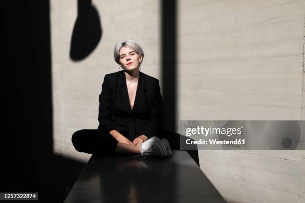 stylish businesswoman wearing elegant suit relaxing on retaining wall with sunlight and shadow in background - portrait shadow stock pictures, royalty-free photos & images