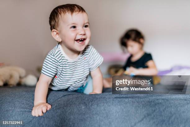 portrait of happy baby girl crawling on  bed while her sister sitting in the background - double bed stock pictures, royalty-free photos & images