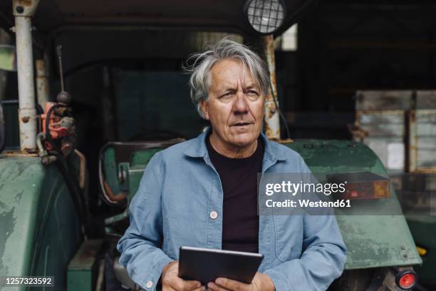 senior man holding tablet on a farm with tractor in barn - digitization stockfoto's en -beelden
