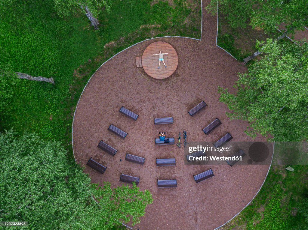 Aerial view of man sitting on bench while woman lying over wooden stage in park
