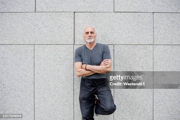 confident senior man with arms crossed standing against wall in city - westend61 fotografías e imágenes de stock