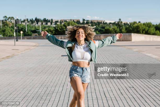 carefree fashionable woman dancing on city street during sunny day - haare schütteln stock-fotos und bilder