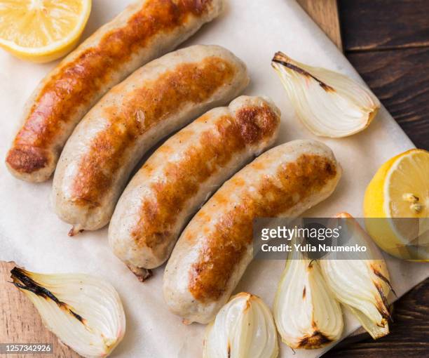 spicy homemade baked sausages with baked vegetables and spices on a brown wooden background. - sausage stock pictures, royalty-free photos & images