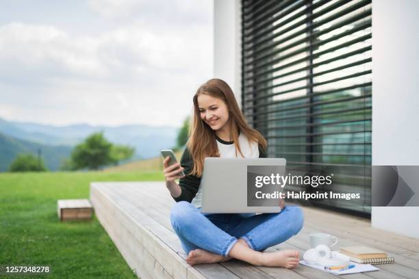 young student with laptop learning outdoors at home, homeschooling concept. - student girl using laptop computer and smart phone stock-fotos und bilder