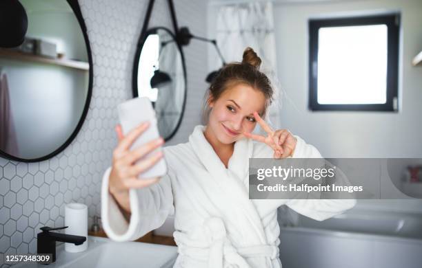 young woman with bathrobe and smartphone in bathroom, taking selfie. - girl in mirror stockfoto's en -beelden