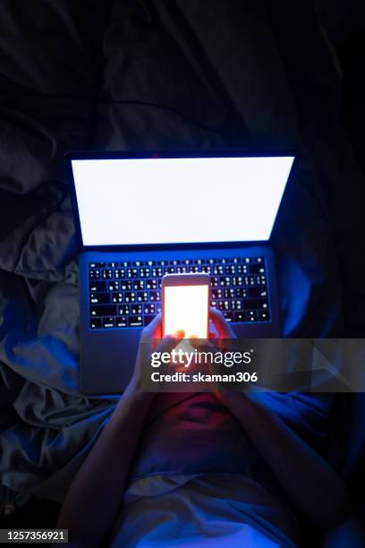 selective focus hand holding smartphone with laptop computer on bed in the night scene - detox bildbanksfoton och bilder