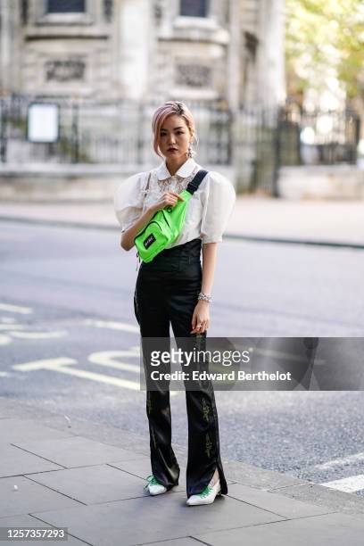 Guest wears a white shirt with large shoulder parts and lace parts, a neon green "M+RC" fanny pack bag, black lustrous flare pants with embroidery,...