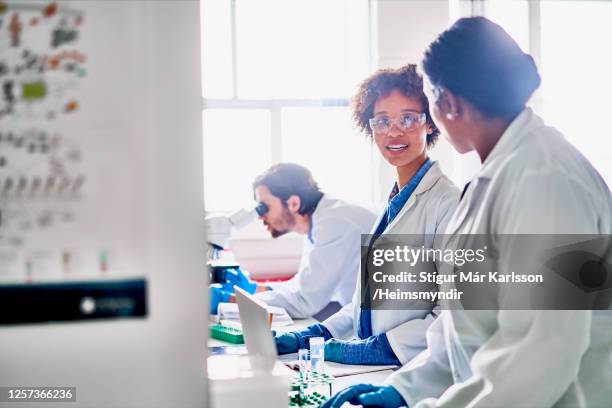 lächelnde wissenschaftler diskutieren gemeinsam im labor über forschung - scientist standing next to table stock-fotos und bilder