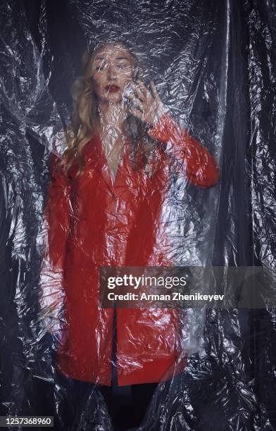blonde woman in a red coat trapped behind a plastic sheet - tin foil hat stock-fotos und bilder