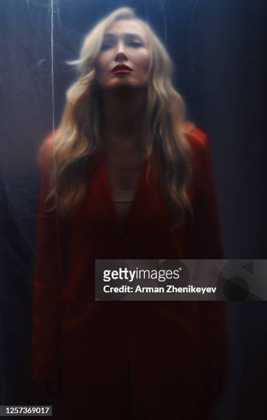 blonde woman in a red coat trapped behind a plastic sheet - mysterious blond woman stock pictures, royalty-free photos & images